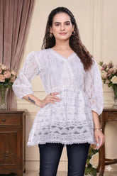 Woman wearing a white lace top in a decorated room with flowers and furniture.