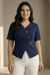 Woman wearing a navy blue top with gold buttons and white pants against a beige wall.