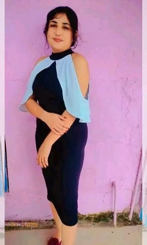 Woman wearing a black dress with a light blue shawl against a pink wall.