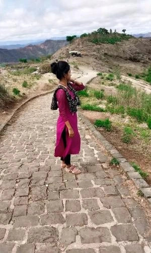 Woman in a pink dress standing on a stone path with a scenic landscape in the background