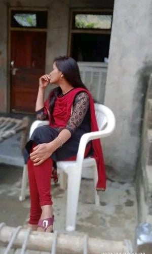 Woman sitting on a white chair wearing a red and black outfit in an outdoor setting.