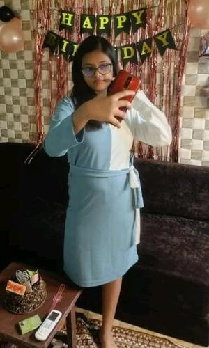 Person in a blue dress taking a selfie with a 'Happy Birthday' banner in the background.