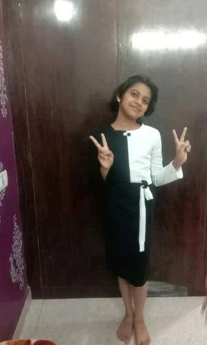 Person wearing a black and white outfit with a belt, standing against a dark wooden door.