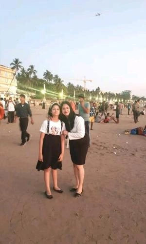 Two women standing on a beach with palm trees and people in the background