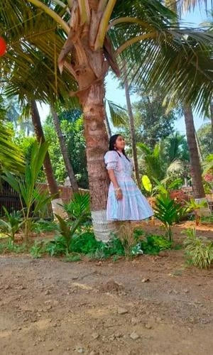 Woman in a white dress standing under a palm tree in a garden setting