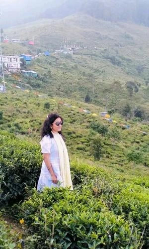 Woman standing in a lush green field with mountains in the background