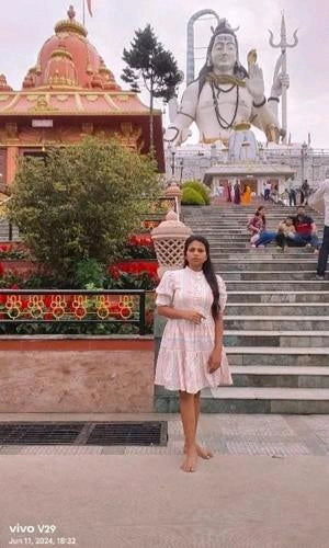 Woman in a dress standing on steps with a large statue and temple in the background