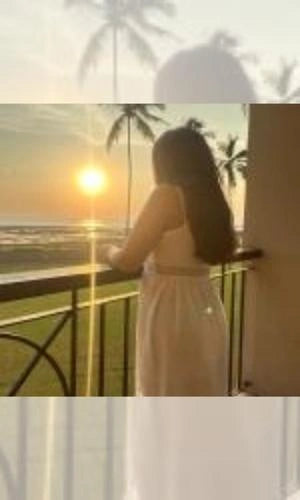Woman standing on a balcony overlooking the ocean at sunset