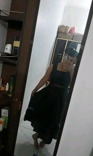 Person wearing a black dress standing in front of a mirror in a room.