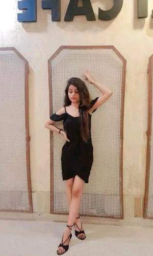Woman in a black dress posing in front of a decorative wall with geometric patterns.