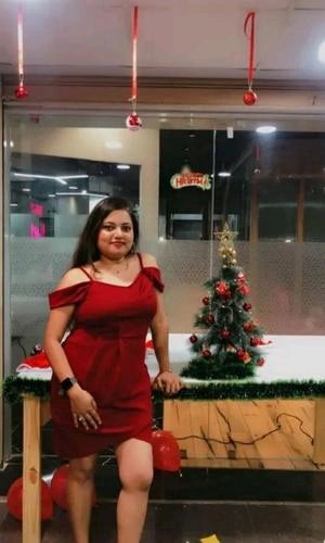 Woman in a red dress standing in front of a Christmas tree and decorations inside a building.