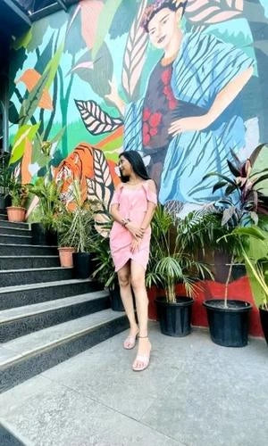 Woman in a pink dress standing on steps with a colorful mural and plants in the background