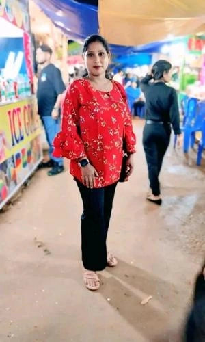 Woman in a red floral blouse and black pants standing in an outdoor market setting.