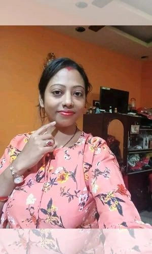Woman in a floral dress posing indoors with an orange wall.