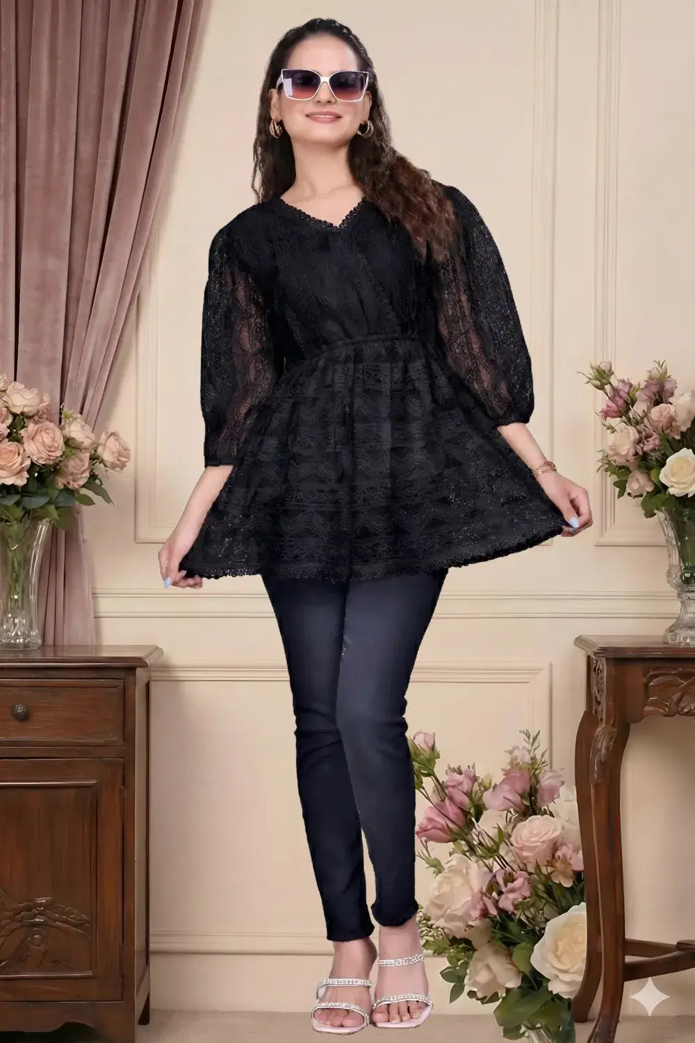 Woman wearing a black dress and sunglasses in an elegant interior setting with flowers.