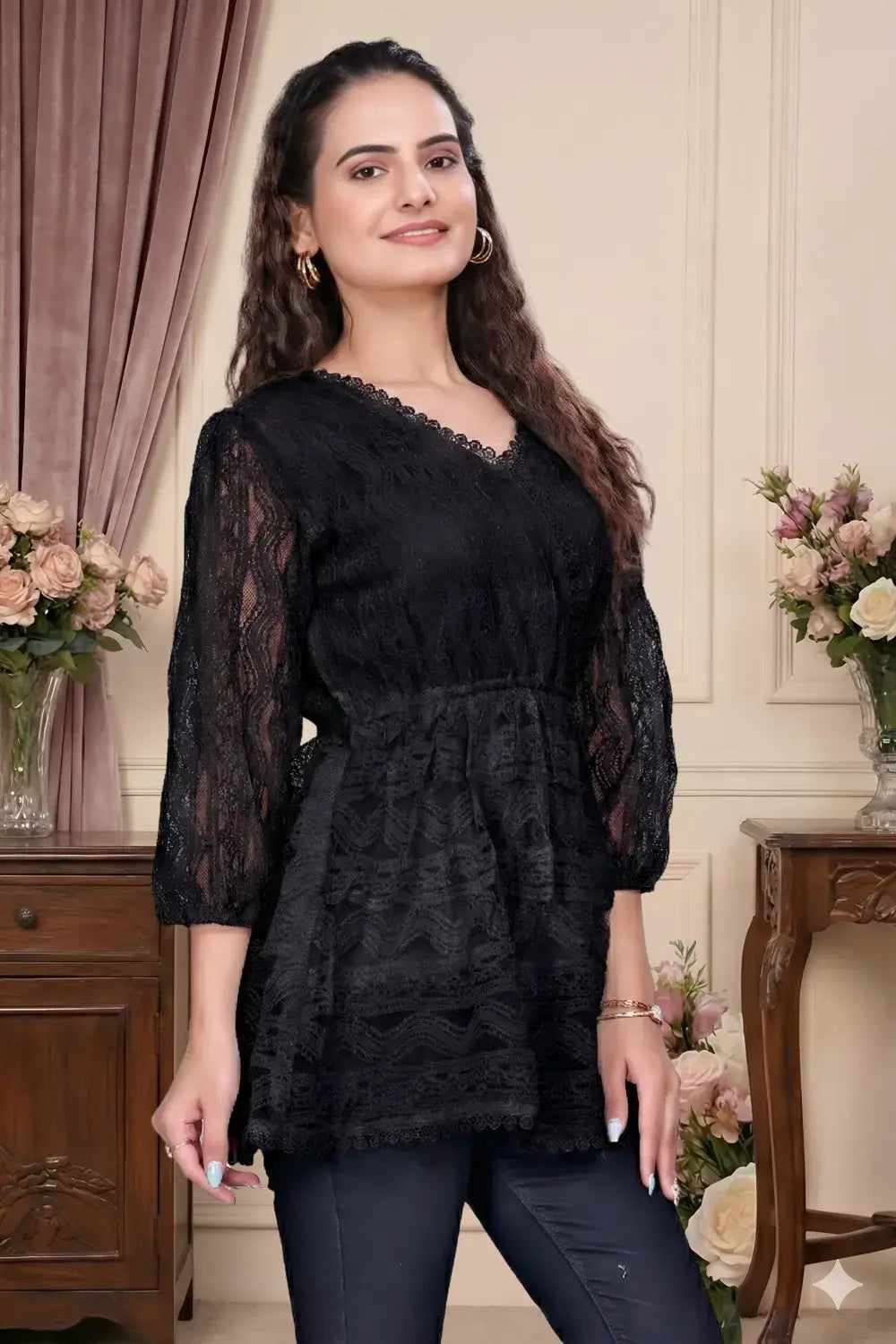 Woman wearing a black lace top in an elegant room with floral arrangements.