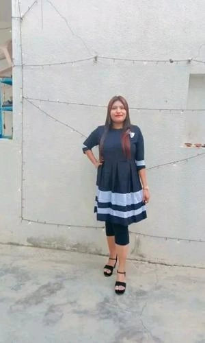 Woman wearing a navy blue dress with white stripes standing against a light gray wall.