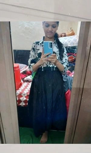 Person taking a mirror selfie wearing a floral top and dark blue skirt in a room.