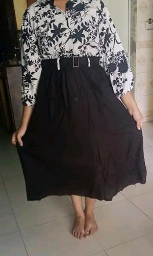 Person wearing a black and white floral top with a black skirt indoors.