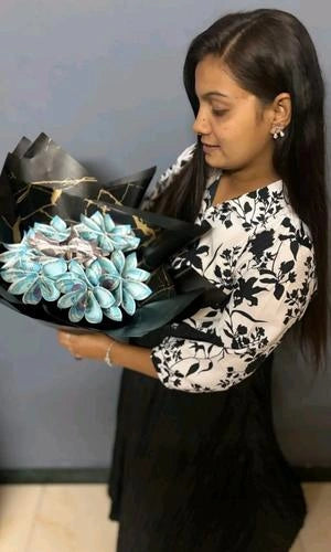 Woman holding a bouquet of flowers with black and gold wrapping against a plain background