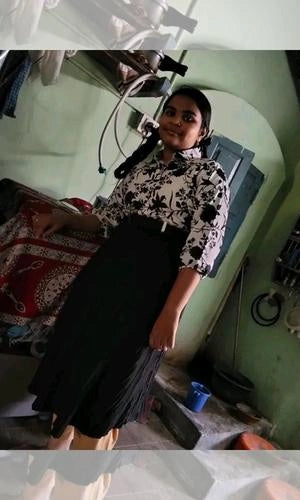 Woman in a black and white floral top and black skirt standing in a room with medical equipment.