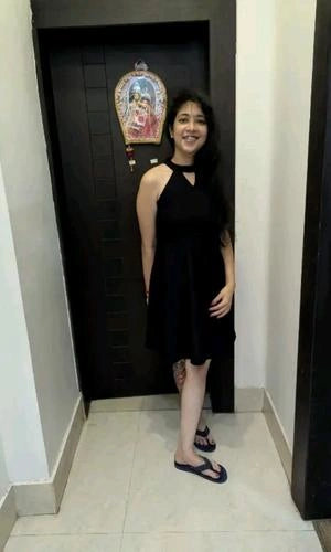 Woman in a black dress standing in a room with a dark door and decorative item.