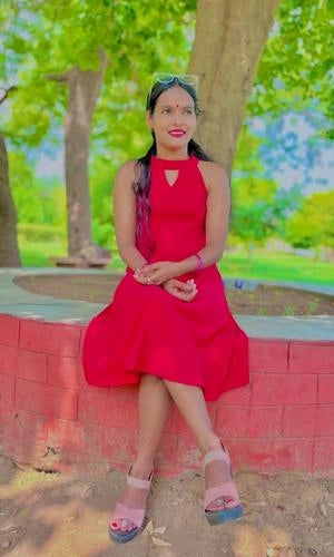 Woman in a red dress sitting on a brick wall with greenery in the background
