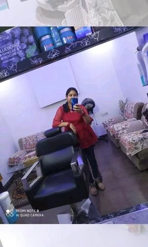 Woman taking a mirror selfie in a salon with a chair and products in the background.