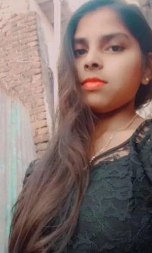 Woman with long hair and orange lipstick standing against a brick wall.