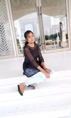 Person sitting on a white bench with a building and garden in the background