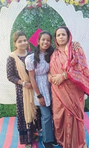 Three women posing together in front of a decorative arch with flowers.