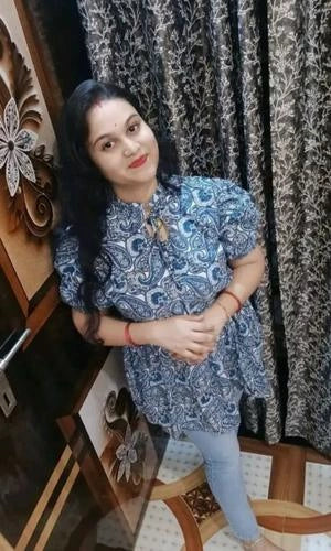 Woman in a blue patterned dress standing in front of a decorative wall.