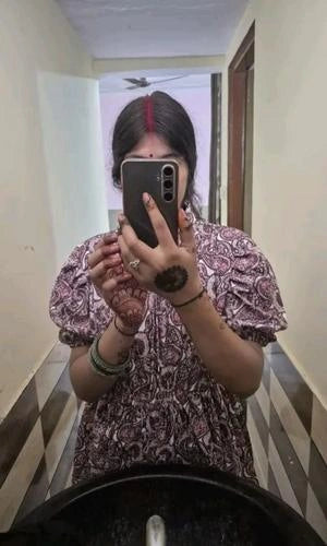 Person taking a mirror selfie in a patterned shirt in a hallway.