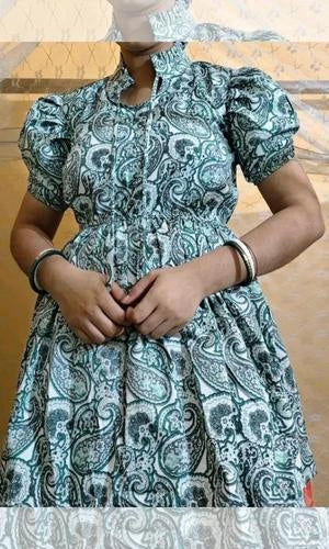 Person wearing a green and white patterned dress with puffed sleeves.