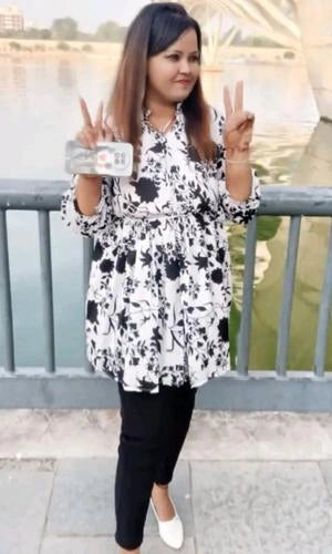 Woman in a black and white floral dress standing by a railing with a blurred background
