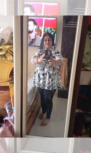 Person taking a mirror selfie wearing a black and white patterned top and dark pants.