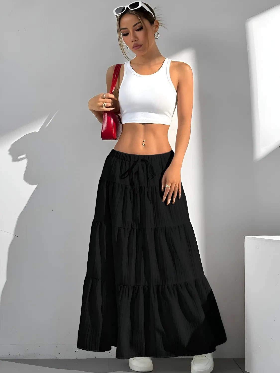 Woman wearing a white crop top and black tiered skirt with a red bag against a gray background