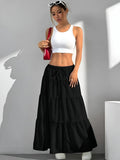 Woman wearing a white crop top and black tiered skirt with a red bag against a gray background