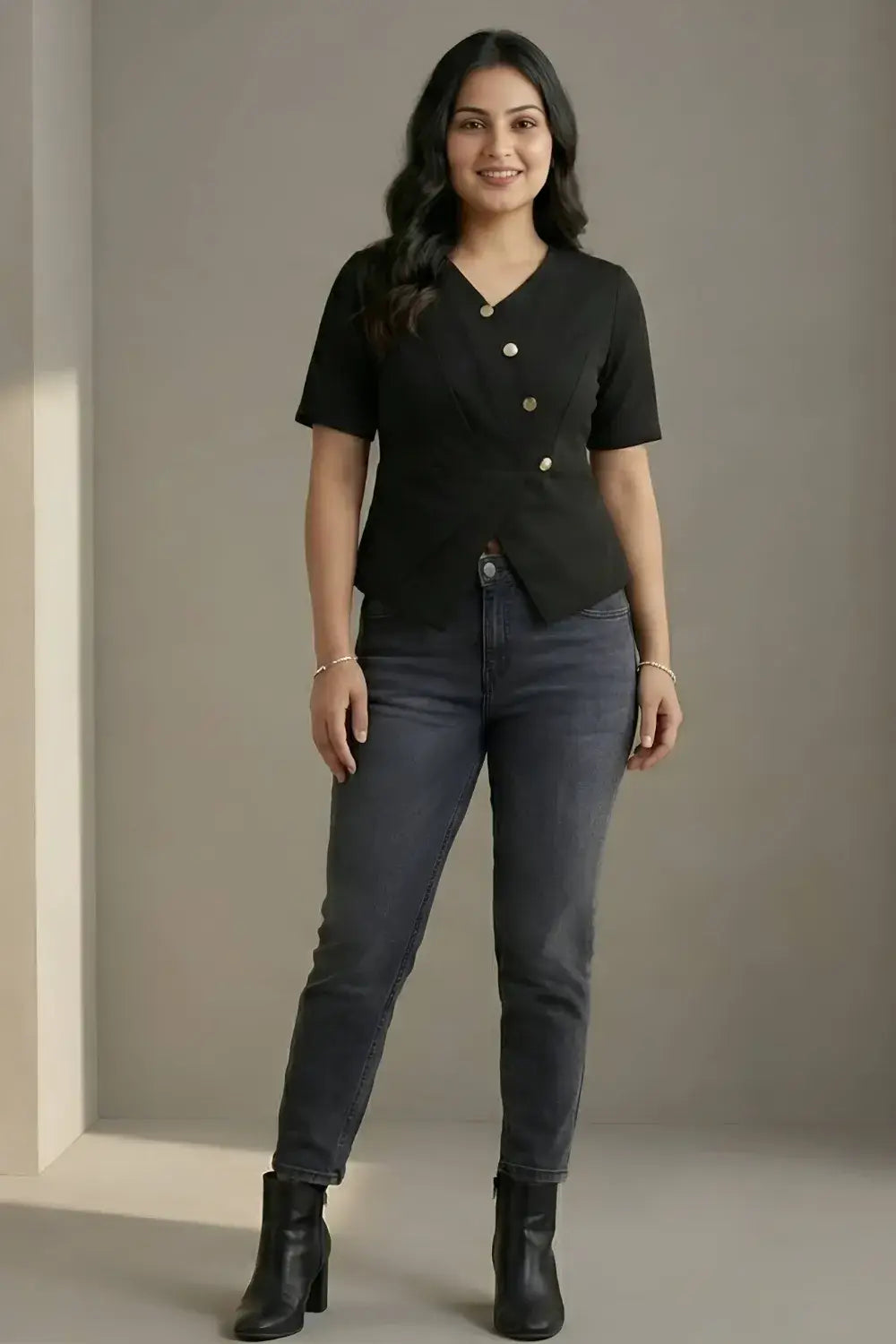 Woman wearing a black top and gray jeans against a plain background