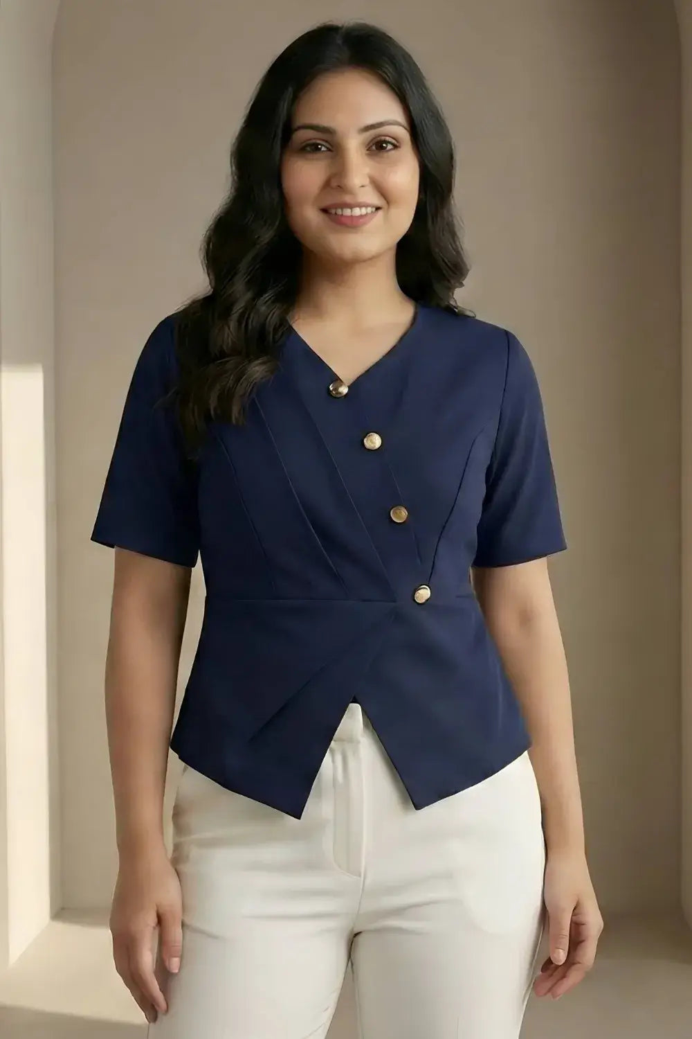 Woman wearing a navy blue top with gold buttons and white pants against a beige wall.