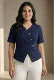 Woman wearing a navy blue top with gold buttons and white pants against a beige wall.