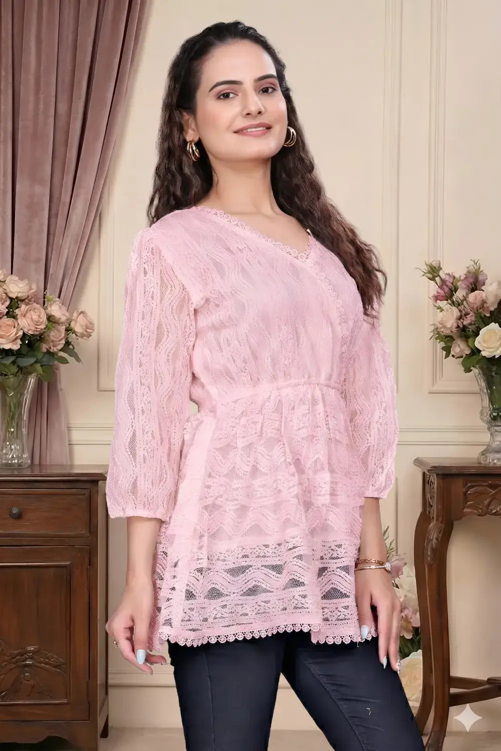 Woman wearing a pink lace top in an elegant room with floral decorations.