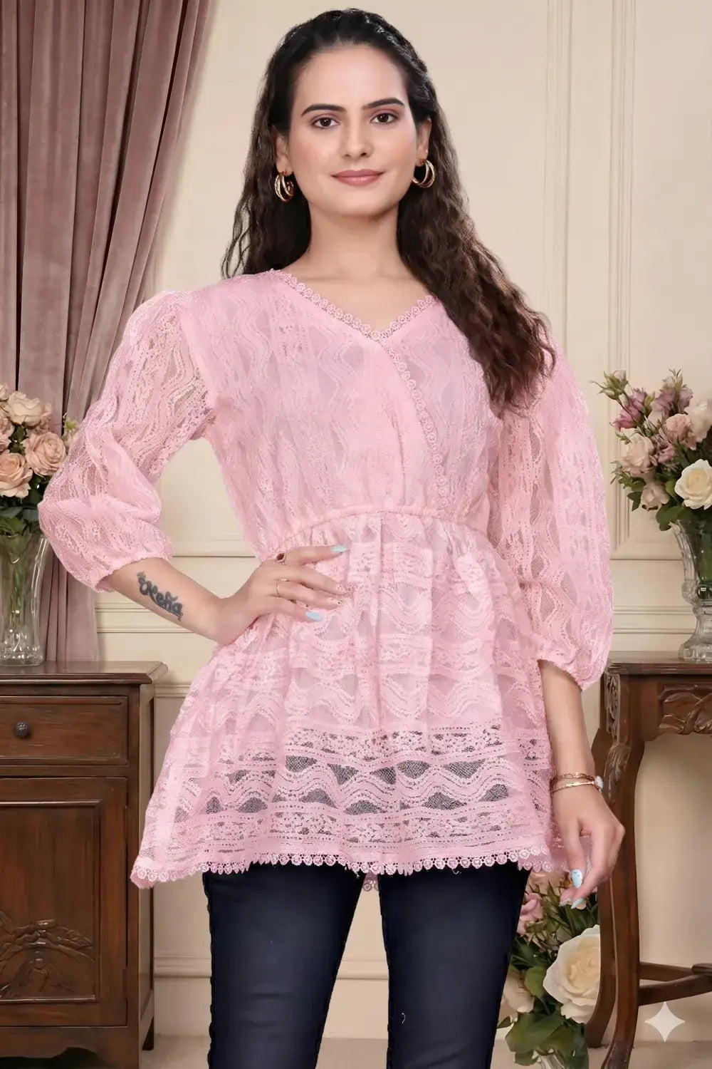 Woman wearing a pink lace top in a decorated room with flowers and furniture.
