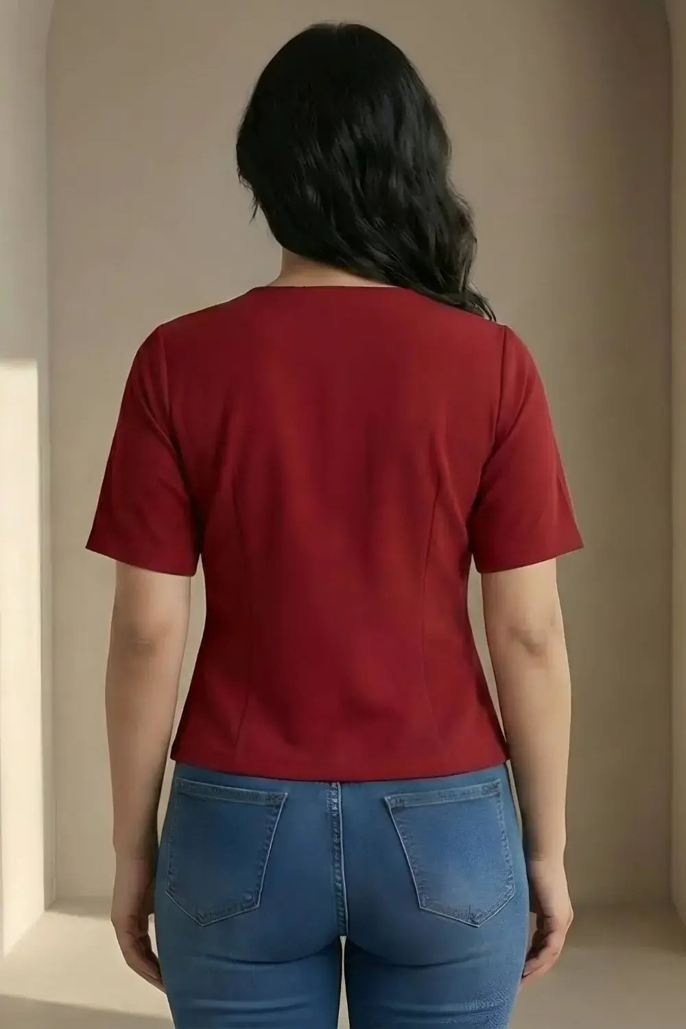 Person wearing a red shirt and blue jeans standing against a beige wall.