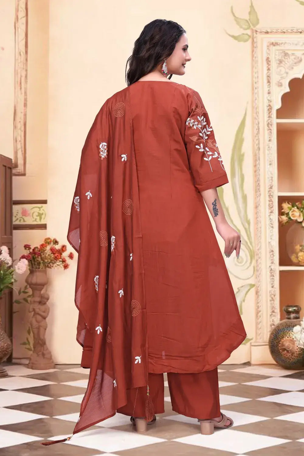 Woman wearing a rust-colored traditional outfit with floral patterns indoors.