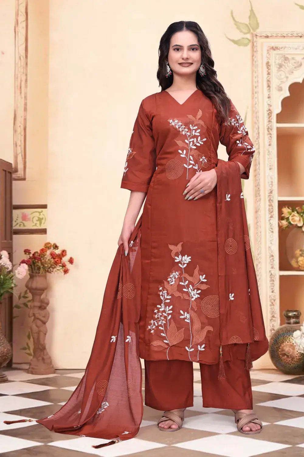 Woman wearing a rust-colored embroidered traditional outfit in a decorated room.