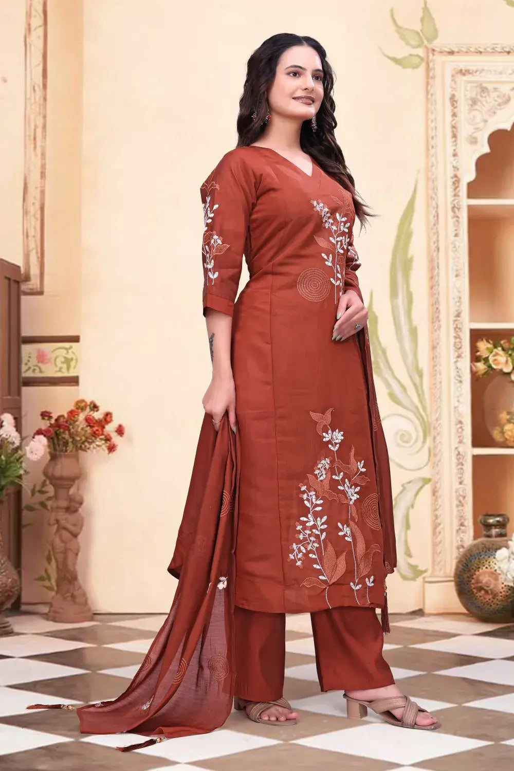 Woman wearing a rust-colored traditional outfit with floral embroidery in an indoor setting.