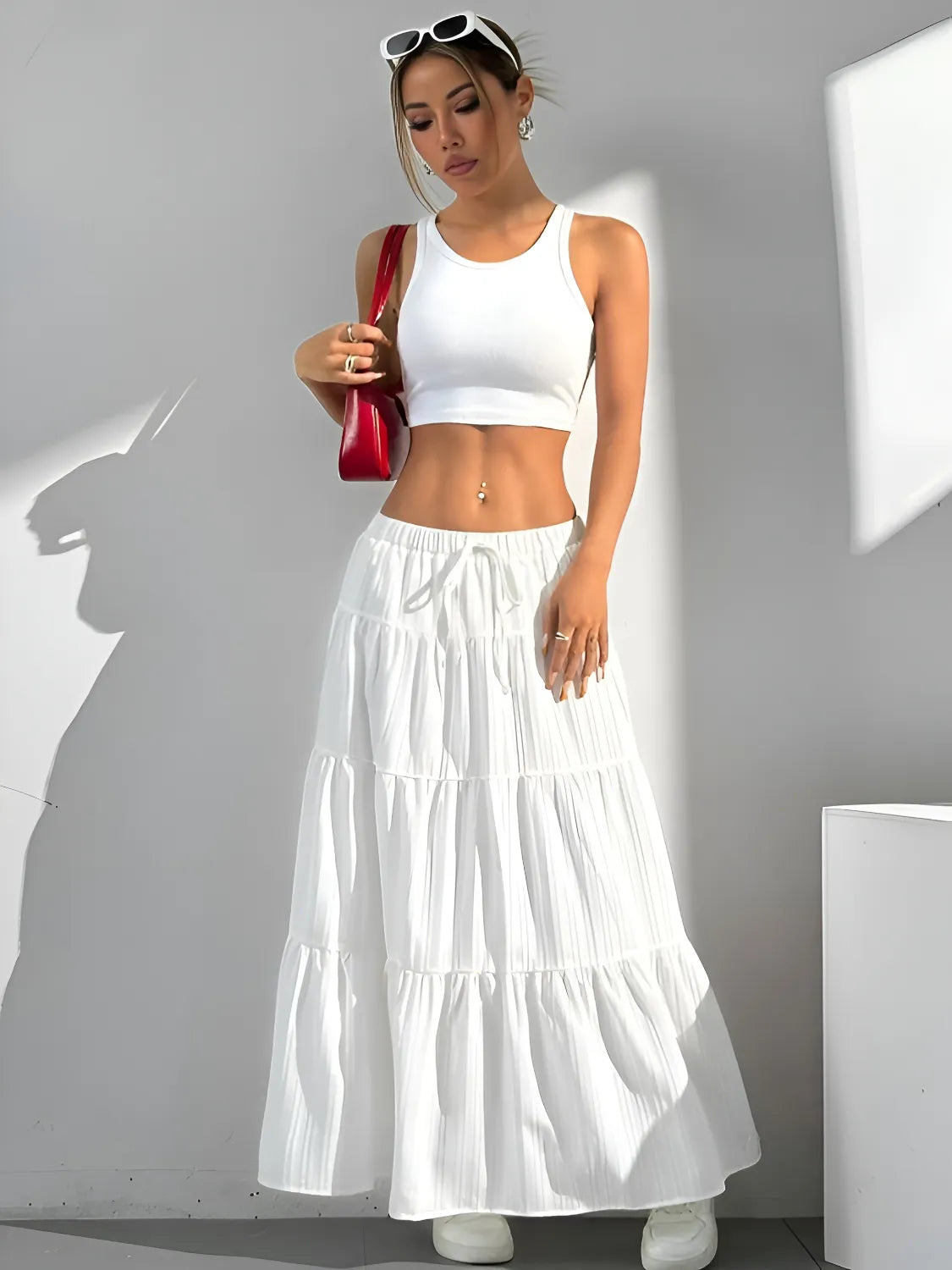 Woman wearing a white sleeveless top and tiered white skirt against a gray background