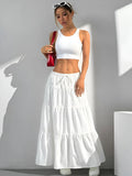 Woman wearing a white sleeveless top and tiered white skirt against a gray background