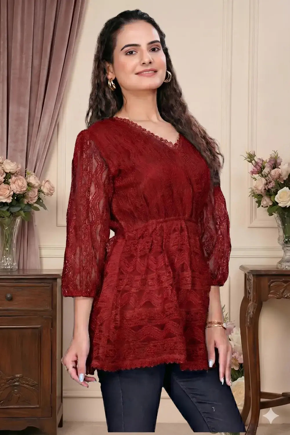 Woman wearing a red lace top in an elegant room with floral arrangements.